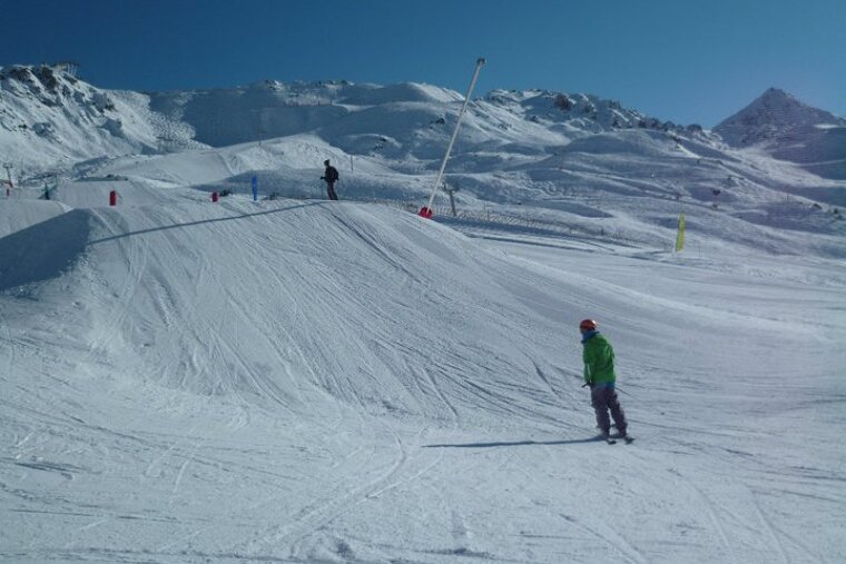 A person in a green jacket is skiing down a snowy slope