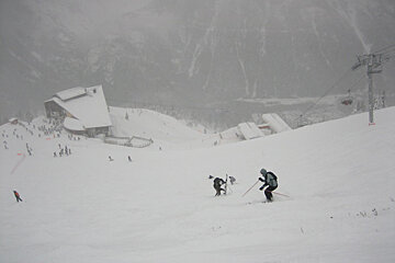 People skiing down a snow covered slope with a ski lift in the background