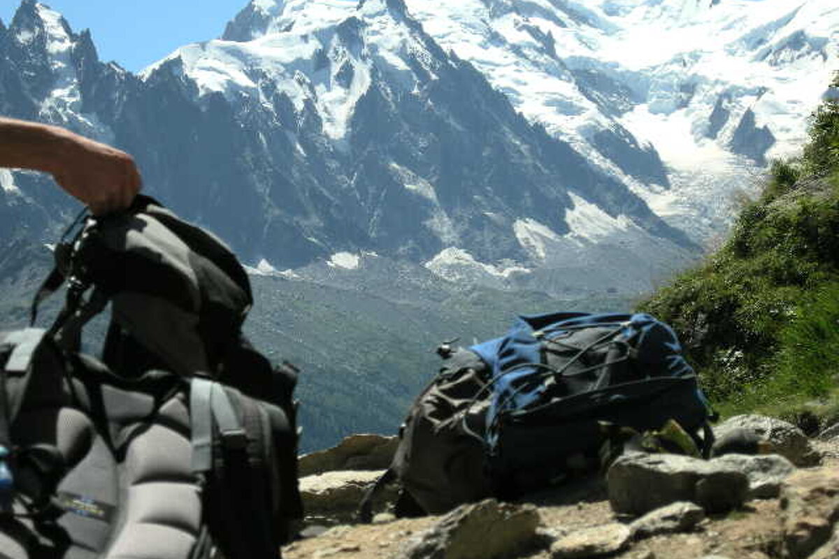 A person holding a backpack in front of a snowy mountain