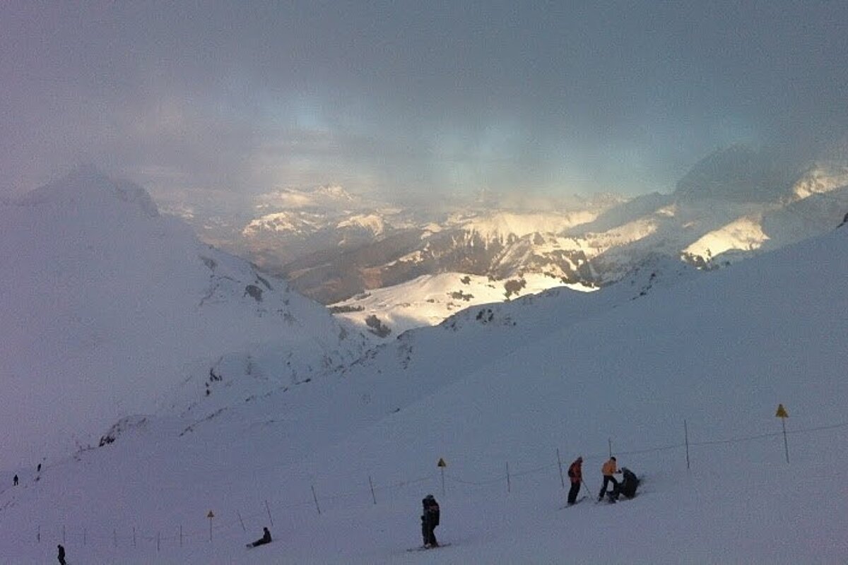 Skiers on piste with cloud and mountains in background