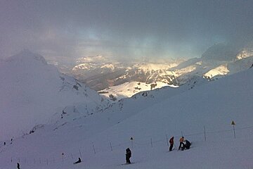 Skiers on piste with cloud and mountains in background