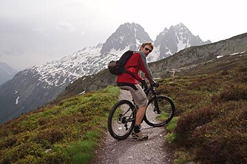 A man riding a bike on a trail with mountains in the background