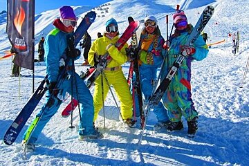 five girls on a piste dressed in one piece ski gear