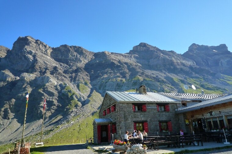 A stone building with red shutters sits in front of a mountain