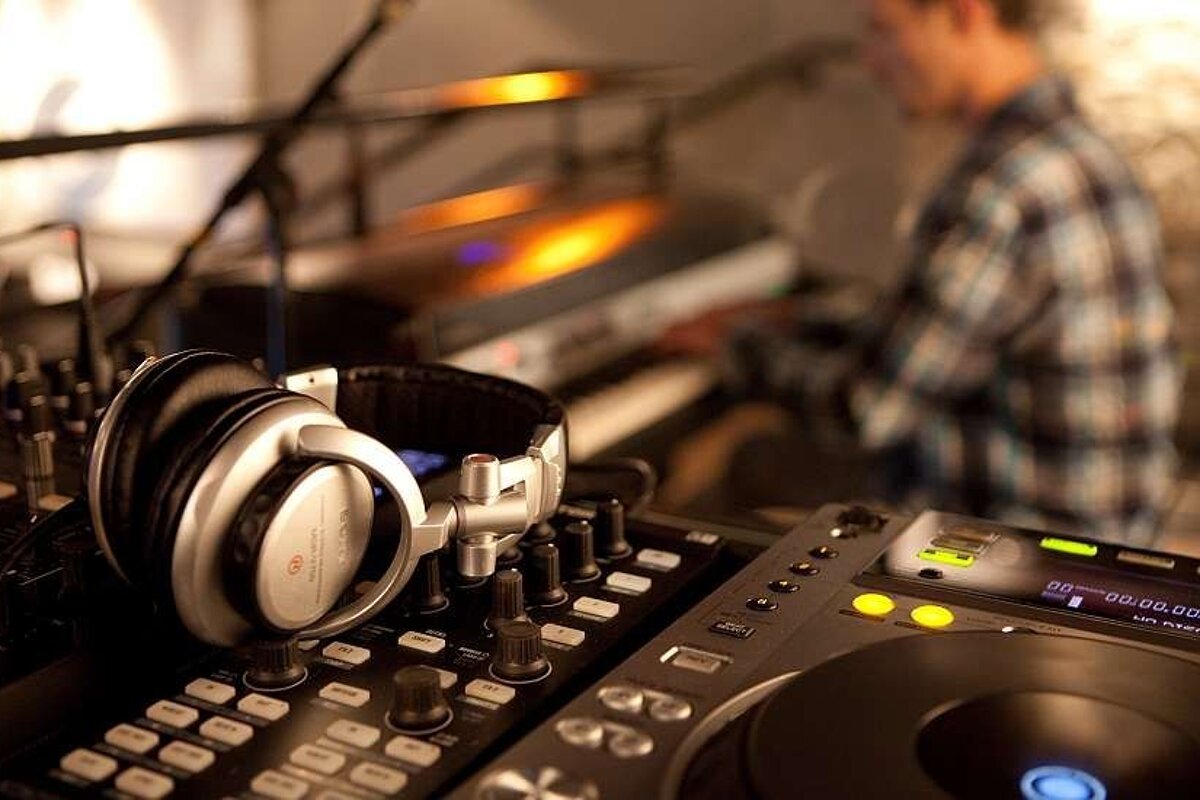 an image of a DJ mixing desk with a man playing keyboards in the background