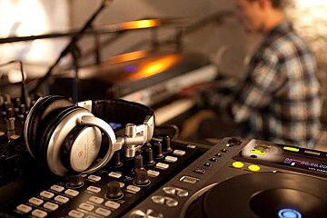 an image of a DJ mixing desk with a man playing keyboards in the background
