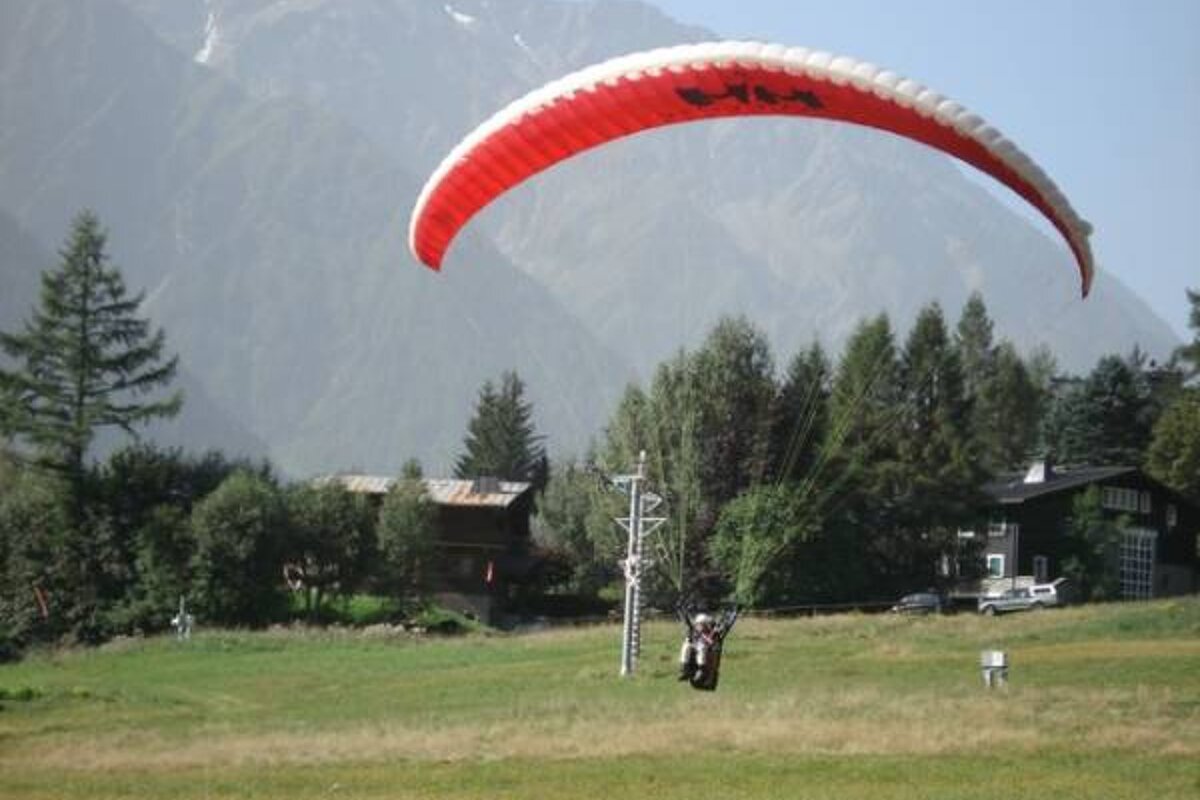 an image of a parapenter landing in a field with a red parachute
