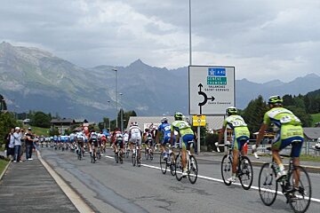A group of cyclists are riding down a road in front of a sign that says geneve