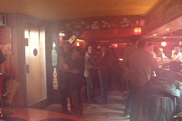 A group of people are dancing in a bar with a bottle of heineken in the background