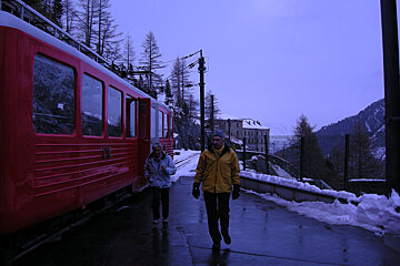 A man in a yellow jacket walks in front of a red train