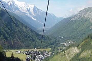 A cable car going down a mountain valley with mountains in the background