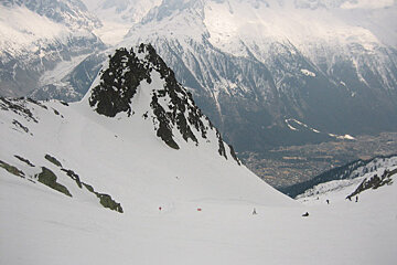 People skiing down a snowy slope with mountains in the background
