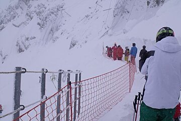 A group of skiers are standing behind a fence in the snow