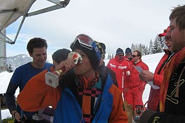 A man in a ski suit drinks from a trophy