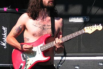 A shirtless man playing a red marshall guitar
