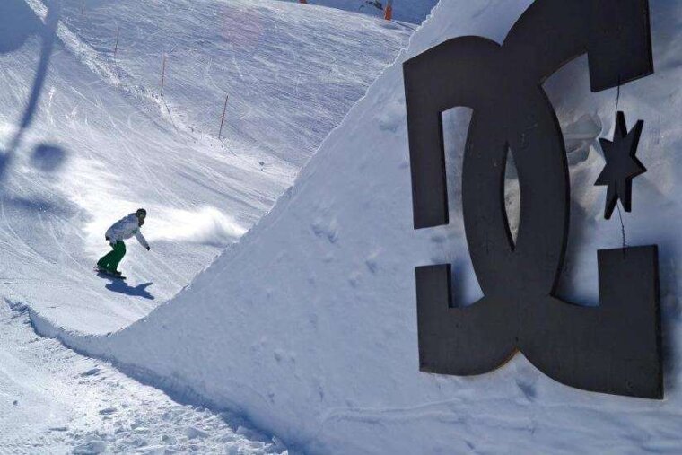 A snowboarder is riding down a snowy slope next to a large dc logo