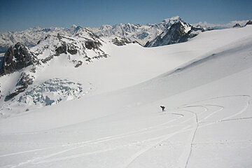 A person skiing down a snowy slope with mountains in the background