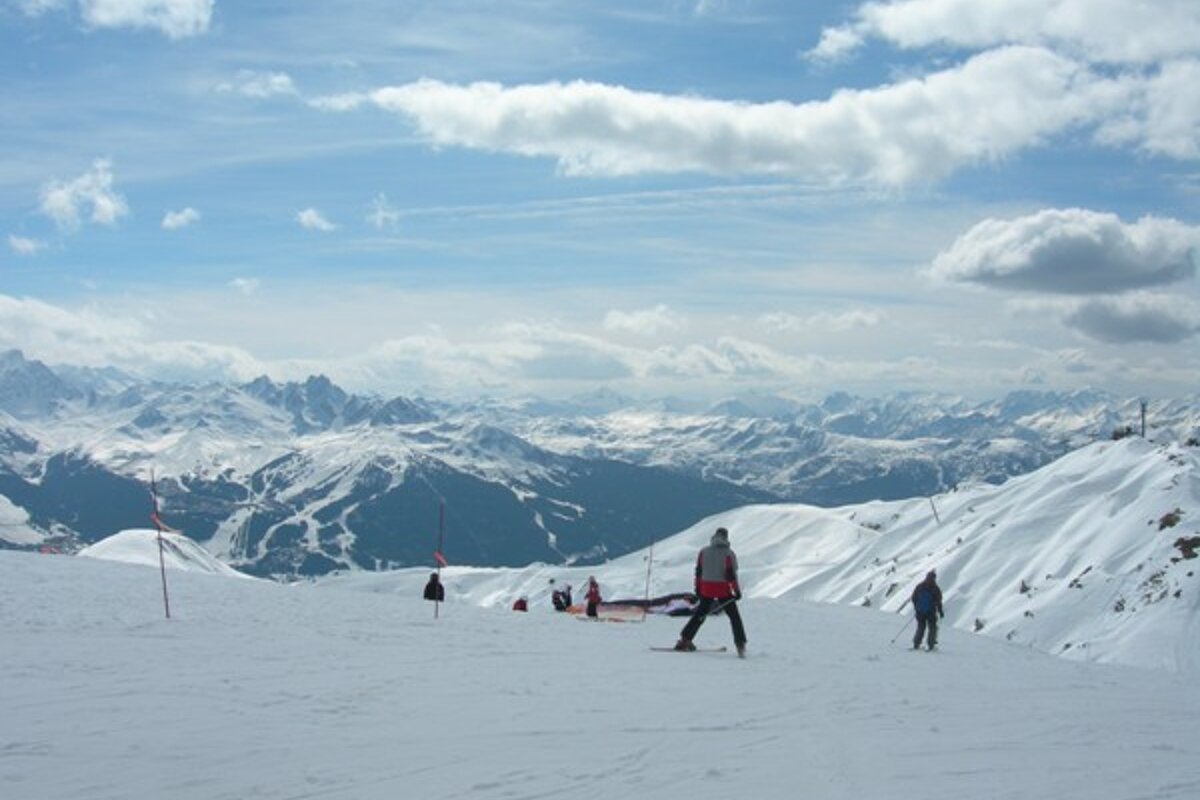 People skiing down a snowy slope with mountains in the background