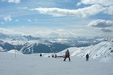 People skiing down a snowy slope with mountains in the background