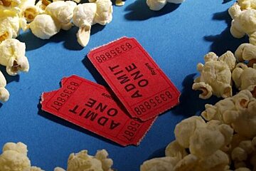 Two red admit one tickets are surrounded by popcorn on a blue surface