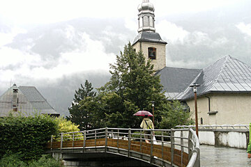 A man with an umbrella walks across a bridge in front of a church