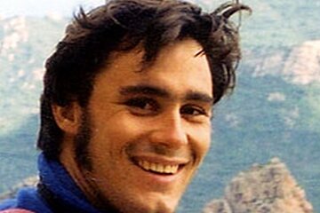 A man with a beard is smiling with mountains in the background