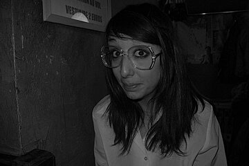 A woman wearing glasses stands in front of a sign that says attention au vin