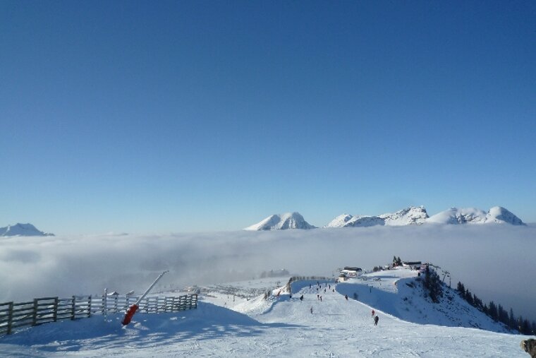 People skiing down a snowy slope with mountains in the background