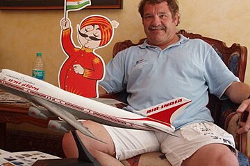 A man sits in a chair holding a model air india plane