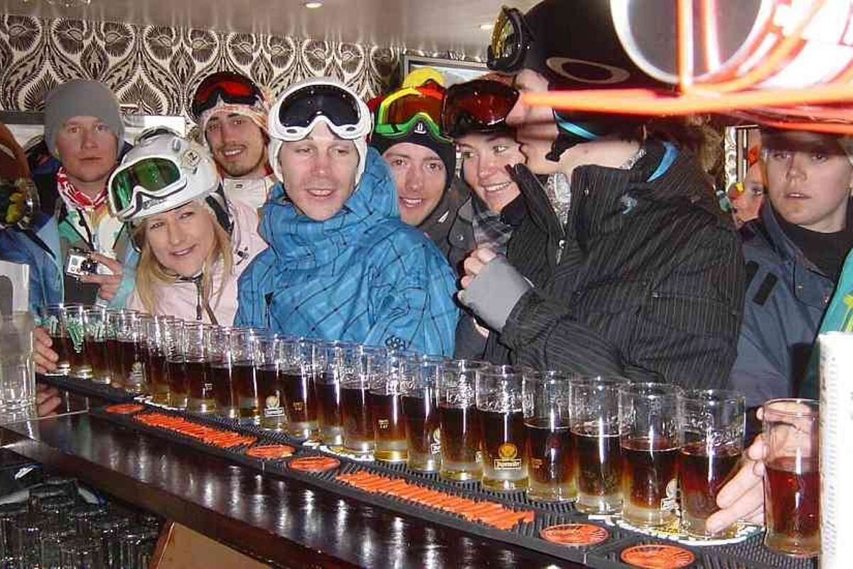 an image of a group in ski gear about to drink a long line of shots