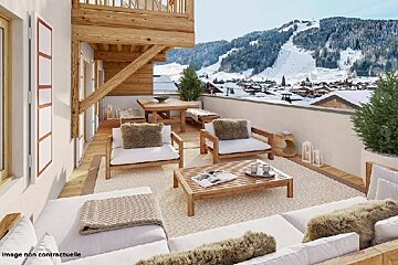 A cozy, luxurious chalet balcony with wooden furniture and plush seating overlooking a snowy ski resort and mountains.