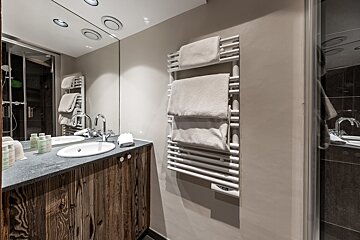 Modern bathroom featuring a rustic wood vanity, white sink, large mirror, and a white heated towel rack on a beige wall.