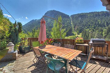 A table and chairs on a deck with mountains in the background