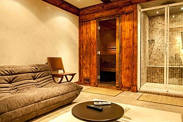 A living room with a couch and a remote in front of a wooden sauna