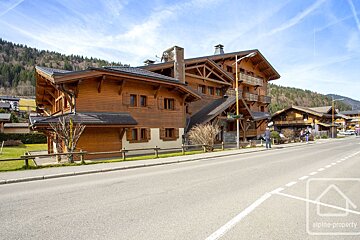 A wooden chalet-style building situated along an asphalt road under a bright blue sky with light clouds.