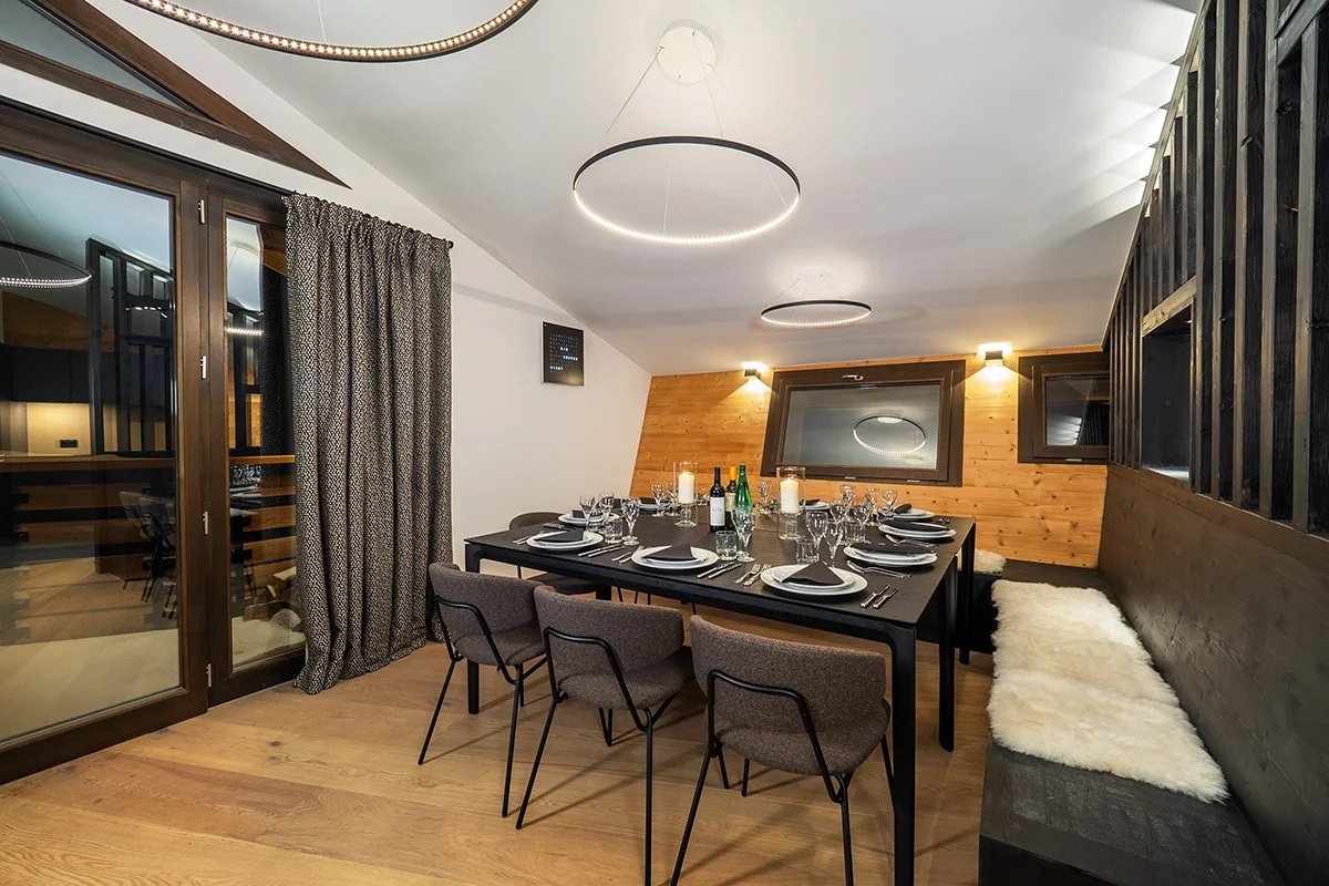 Modern dining room in a chalet, featuring a set table, unique circular hanging lights, and wood paneled walls.