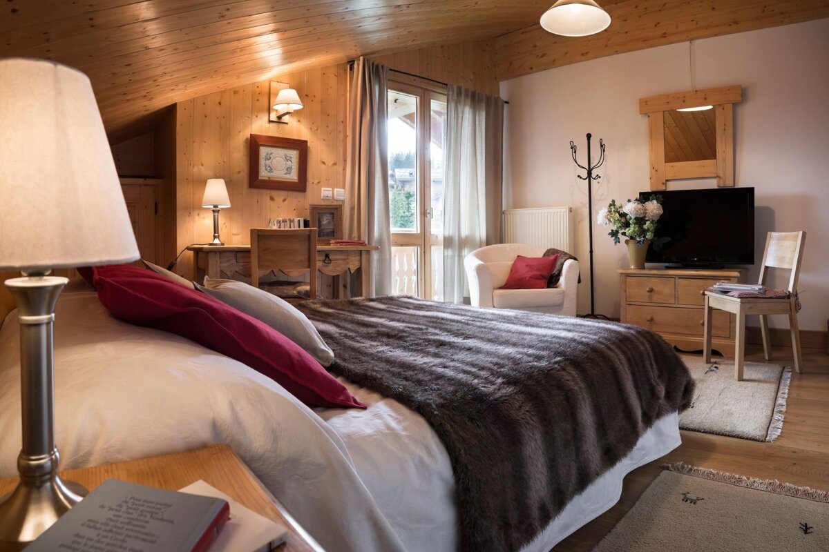 A warm, wood-paneled bedroom features a large bed with a faux fur throw, rustic furniture, and a balcony. Inviting chalet style.