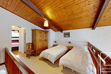 A cozy loft bedroom featuring a wooden vaulted ceiling, two single beds, a wooden wardrobe, and a railing overlooking the floor below.