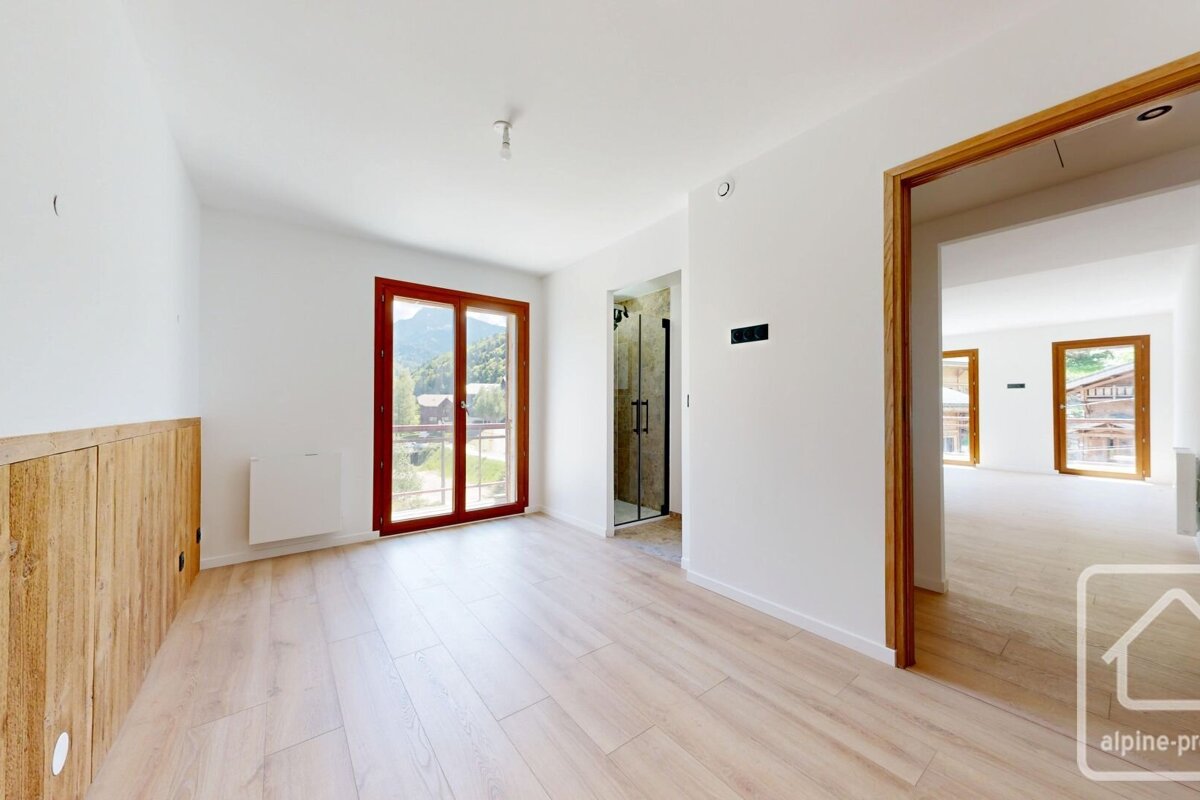 A bright, empty room featuring white walls, light wood flooring, a mountain-view window, rustic wood paneling, and a doorway to another area.