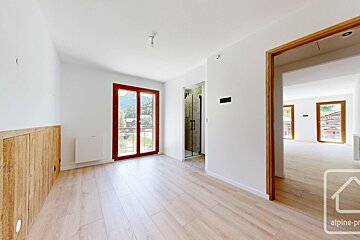 A bright, empty room featuring white walls, light wood flooring, a mountain-view window, rustic wood paneling, and a doorway to another area.