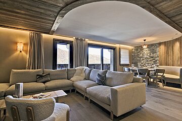 Chic modern chalet living and dining area with a plush sofa, mountain views, and warm wood and stone decor.