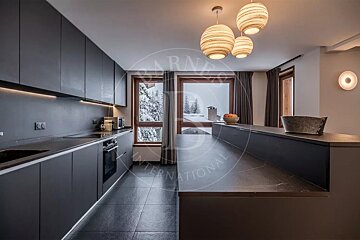 Sleek, modern dark grey kitchen with integrated appliances, under-cabinet lighting, and spherical pendant lamps, featuring a snowy outdoor view.