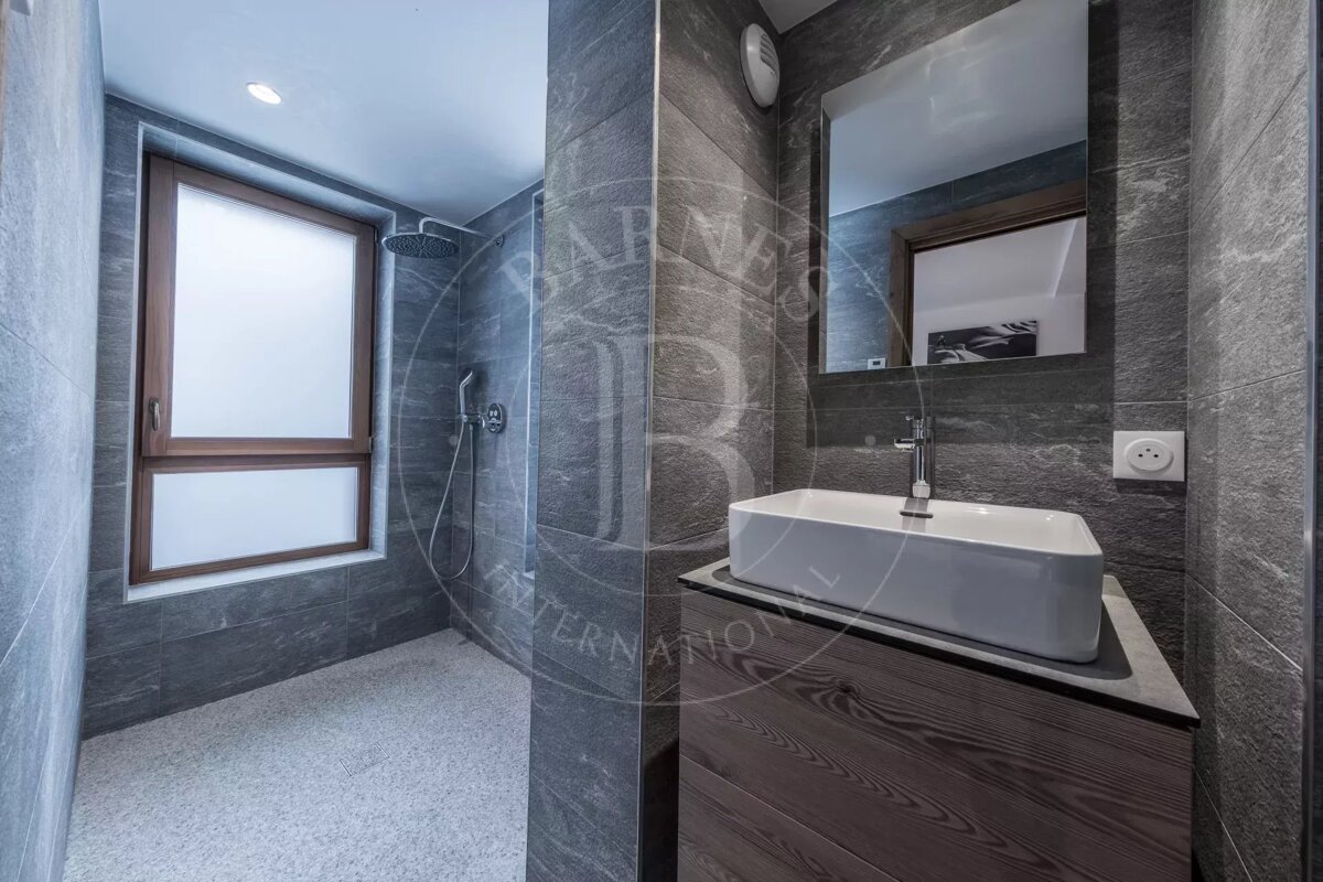 Modern grey-tiled bathroom featuring a walk-in shower with a frosted window, a white rectangular sink on a wooden vanity, and a large mirror.
