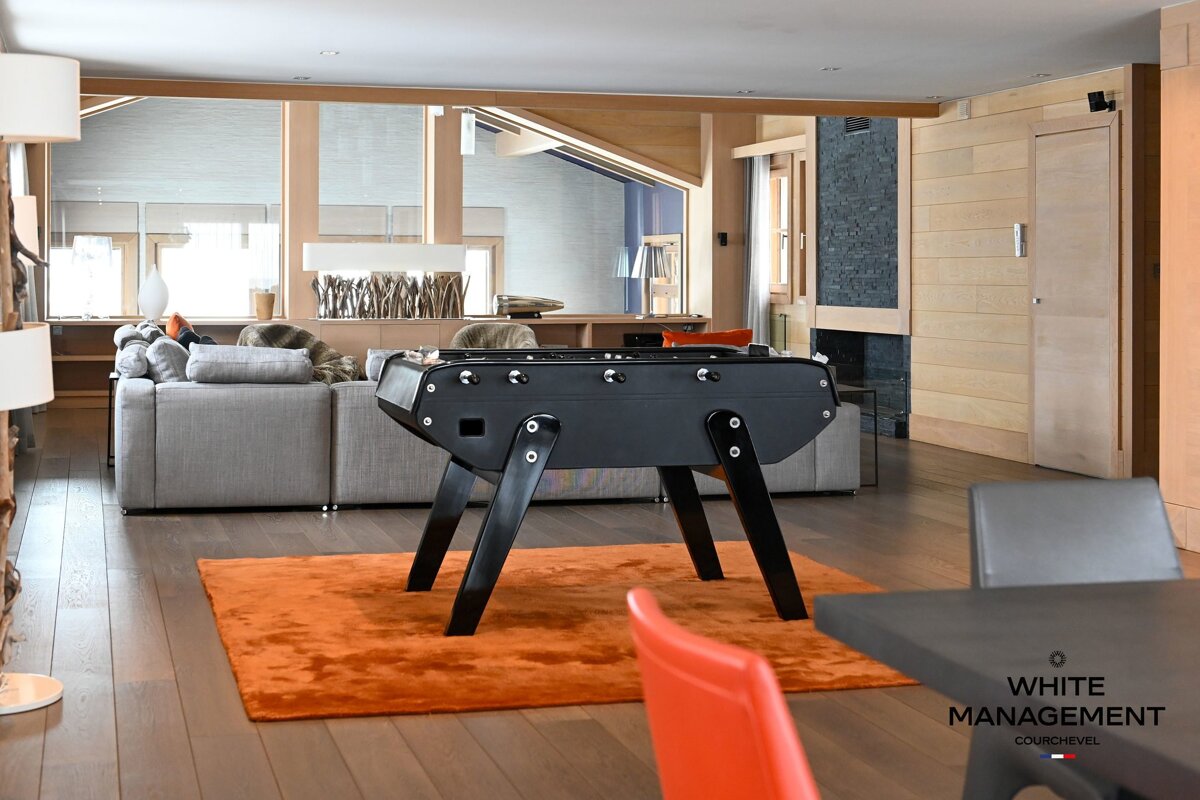 Modern living room featuring a black foosball table on an orange rug, next to a grey sectional sofa.
