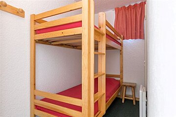 A bunk bed with red sheets in a small room