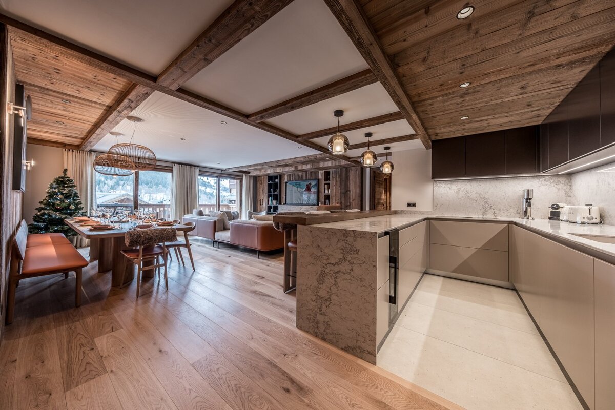 Cozy, luxurious open-plan chalet. Features rustic wood beams, modern kitchen, dining & living areas. Christmas tree and mountain views add to the festive ambiance.