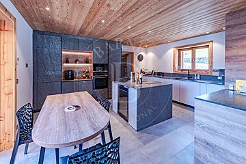 Modern chalet kitchen and dining room with a wood ceiling, grey cabinetry, a central island, and an oval wooden dining table.