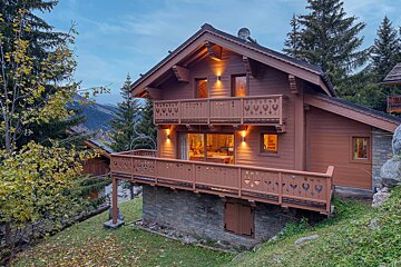 A large wooden house with a balcony and trees in the background