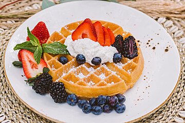 A waffle with strawberries blueberries and whipped cream on top