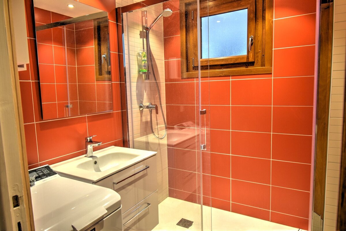 A bright bathroom with vibrant orange tiled walls, a glass walk-in shower, a white sink vanity, and a mirror.